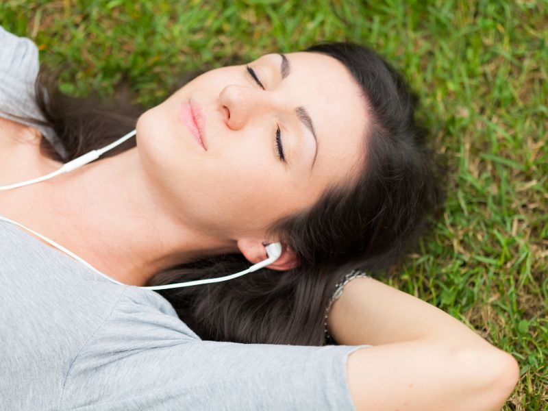 Muzyka relaksacyjna i jej charakterystyka. Na zdjęciu kobieta w słuchawkach na trawie.